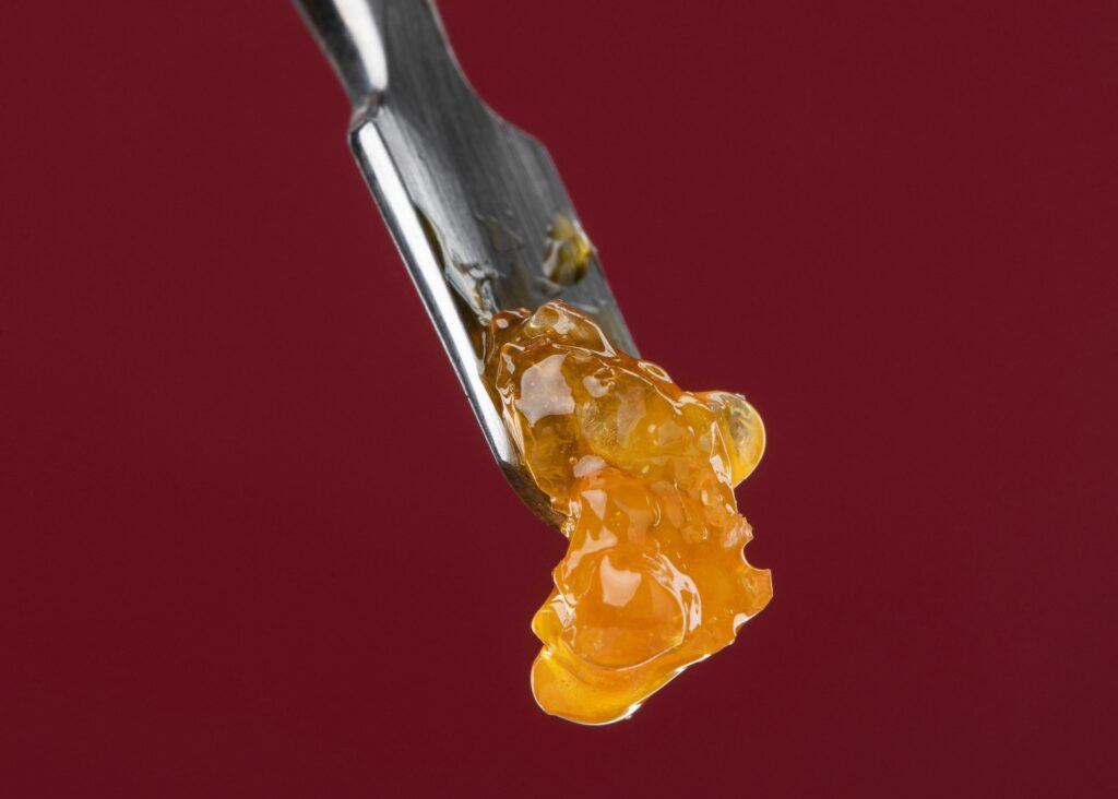 Glossy amber cannabis concentrate on the tip of a metal dab tool against a dark red background