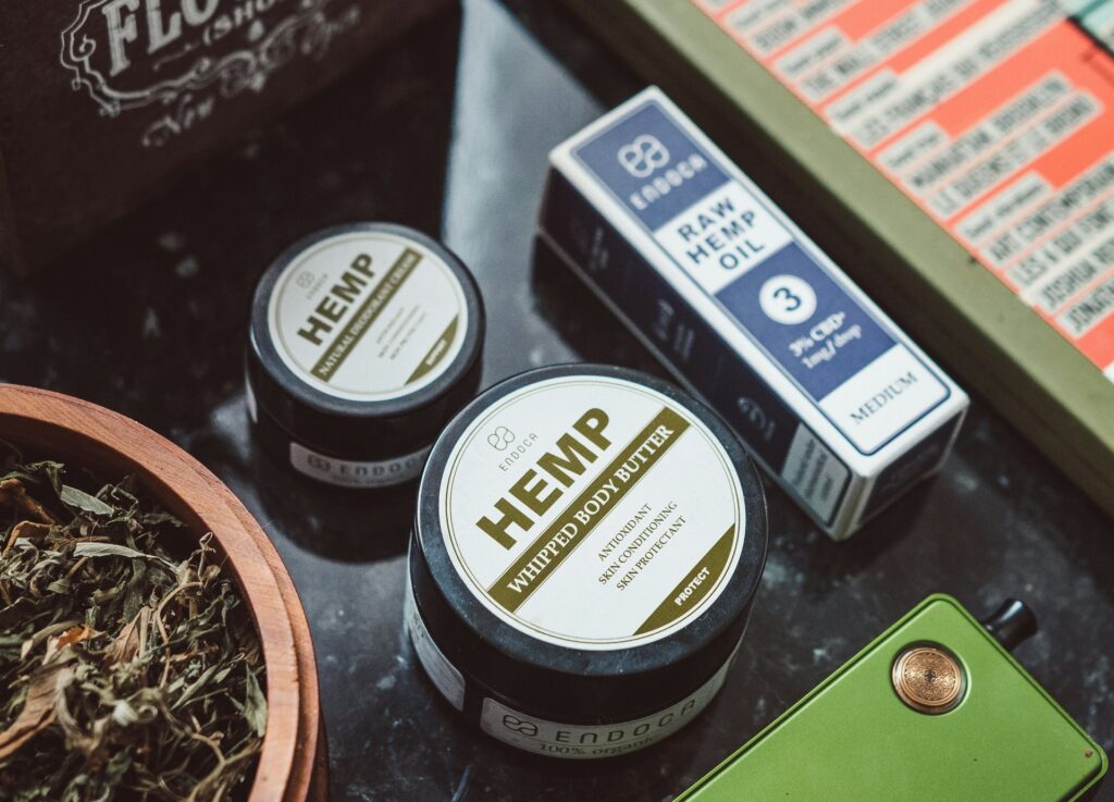 Jars of hemp body butter and cream beside a box of hemp oil and a bowl of dried cannabis, showing cannabis topicals