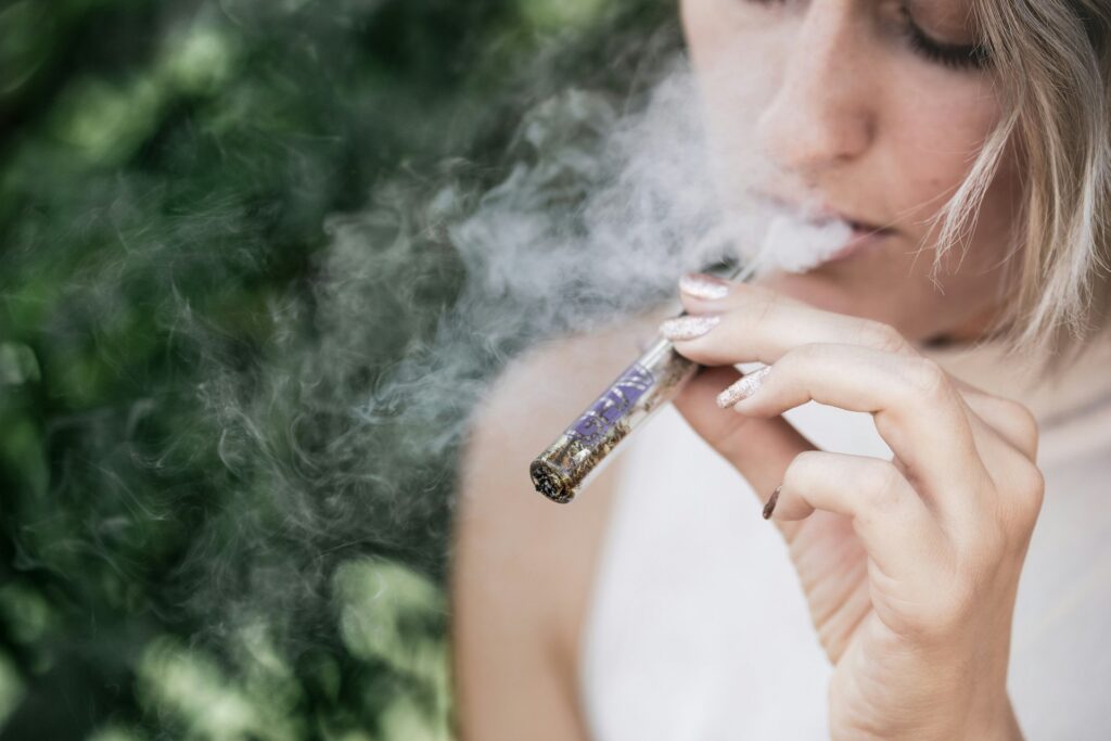 Woman exhaling smoke while holding a glass blunt filled with cannabis flower